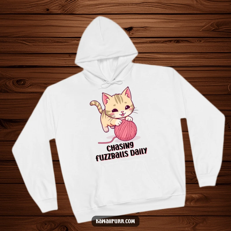 Funny playful cat with a twitching tail, pouncing on a rolling ball of yarn, on a warm hoodie. Humorous and snuggly activewear.
