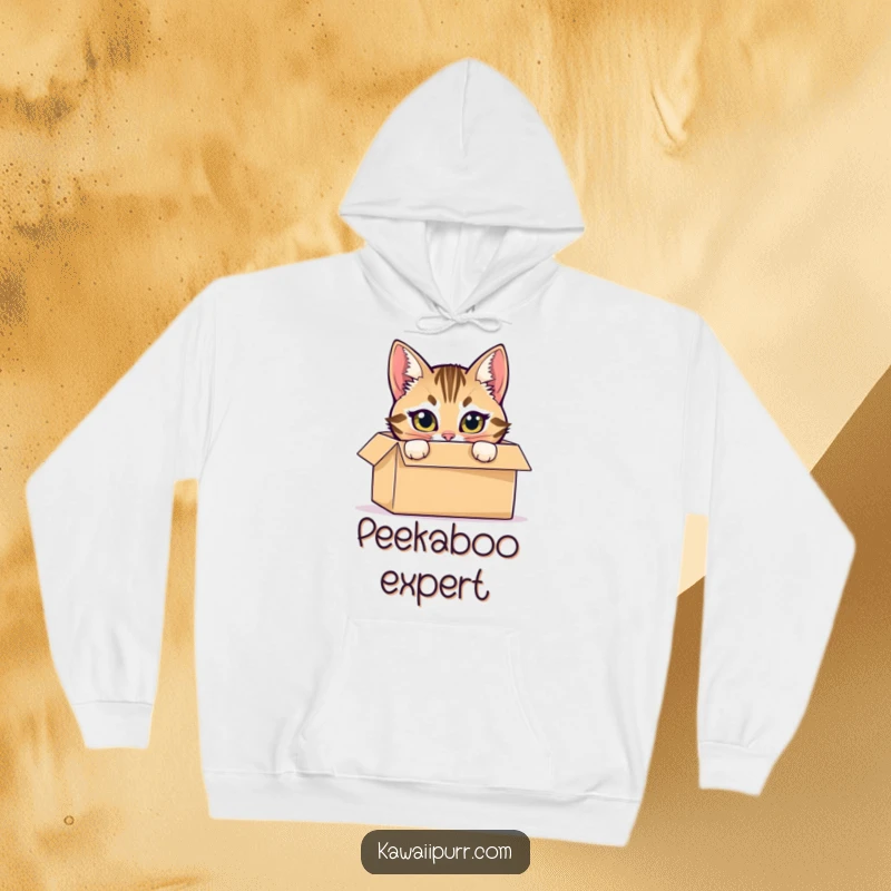 Funny hoodie with a mischievous tabby cat hiding inside a cardboard box, peeking out with bright eyes.